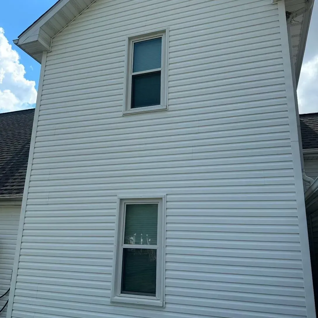 White vinyl-sided house with two windows on the side against a blue sky.
