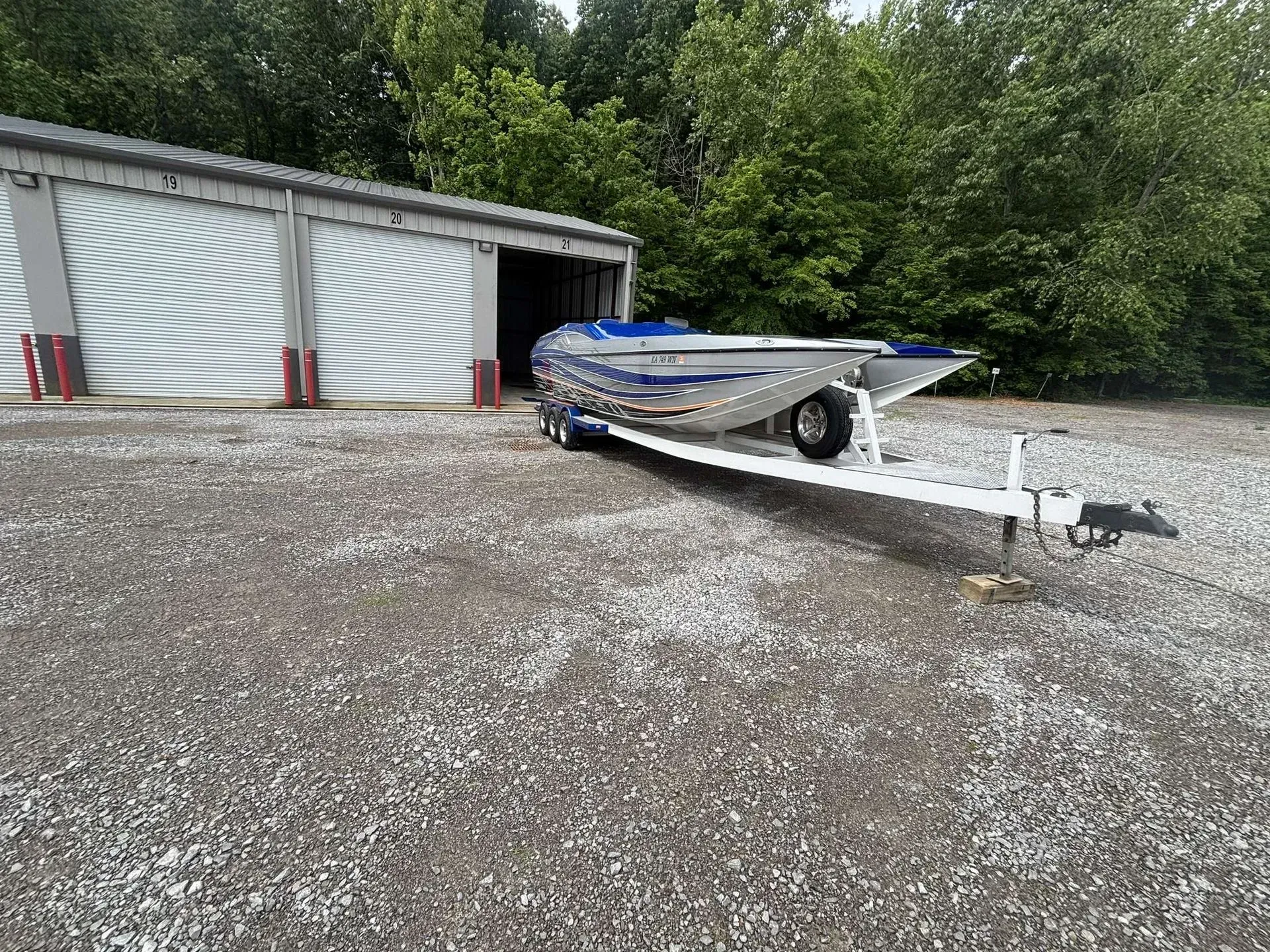 Boat on a trailer outside a storage unit building. Silver boat with blue accents.