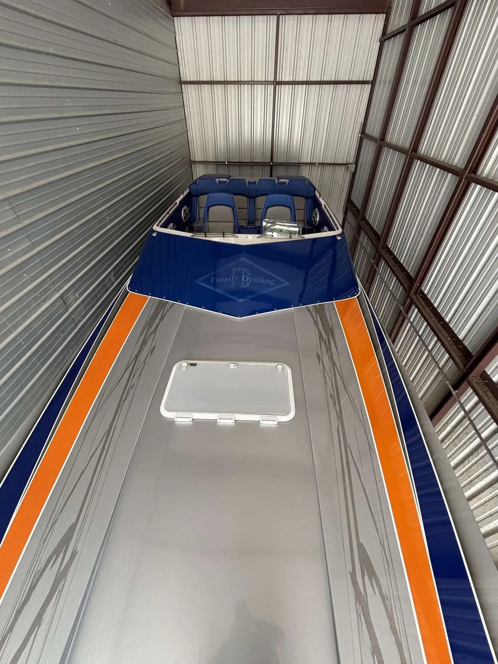 A silver speedboat with orange and blue stripes is stored in a metal building.