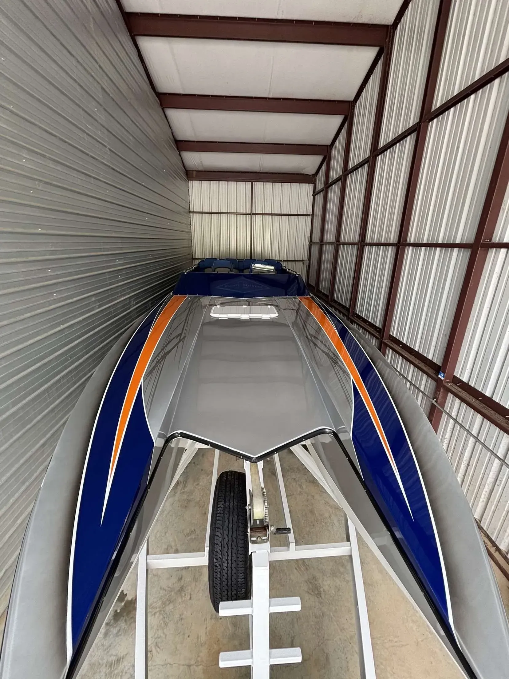 A silver and blue speed boat on a trailer inside a storage unit. Orange stripes on the boat.