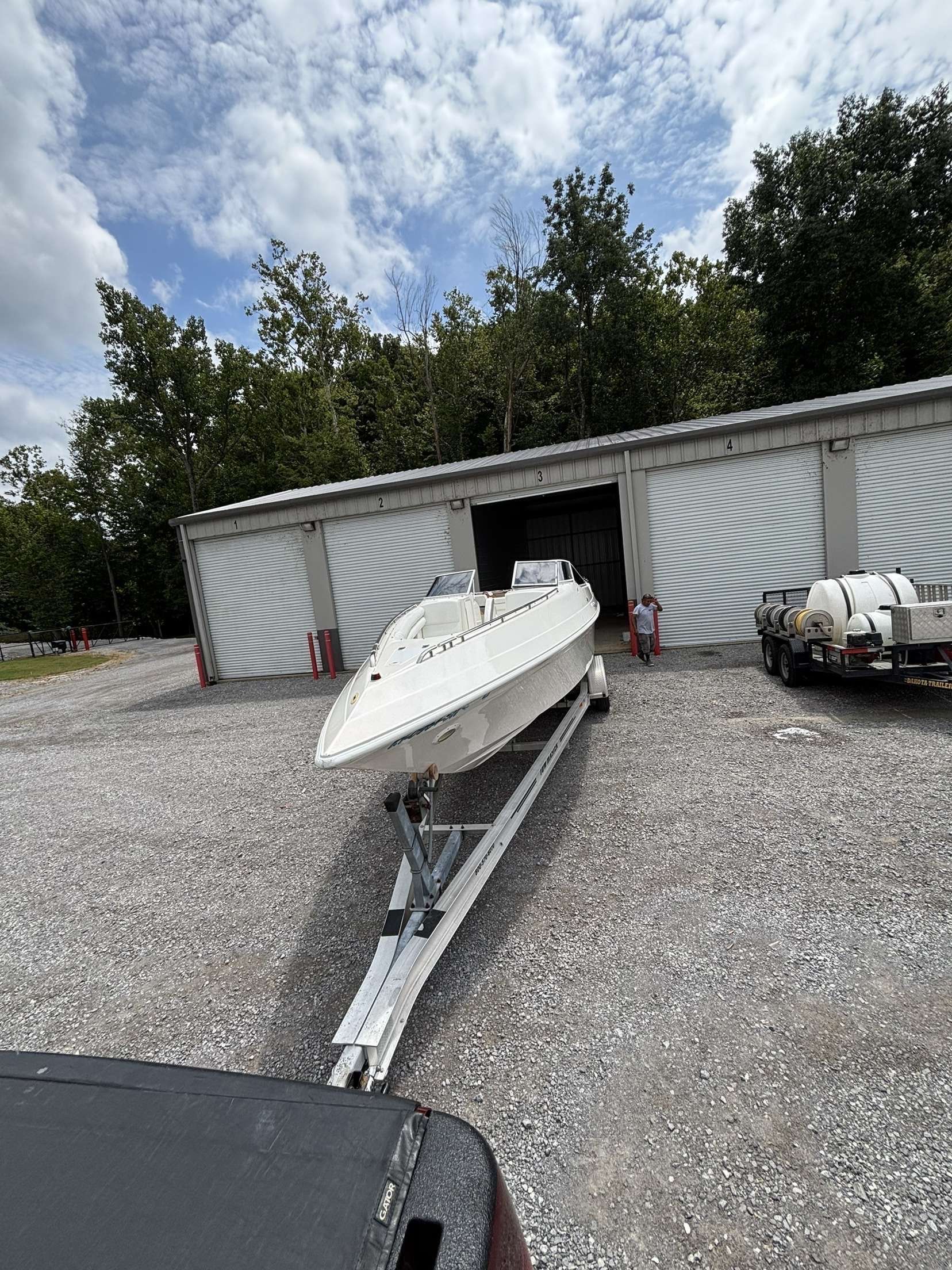 White boat on a trailer in front of a storage building on a gravel lot under a cloudy sky.