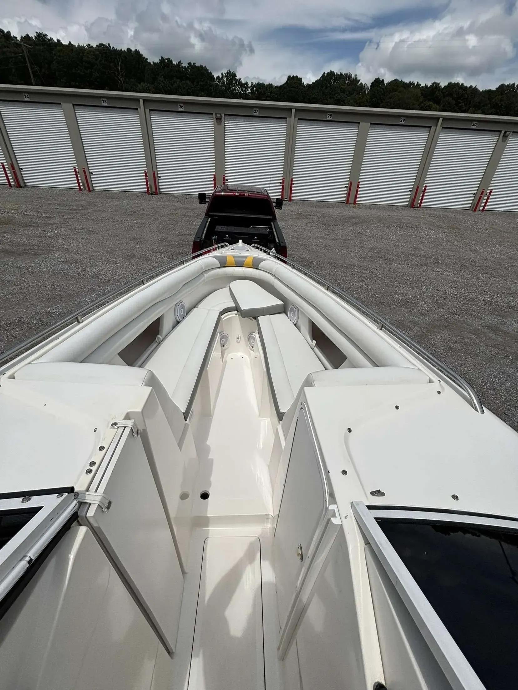 White boat on gravel, facing a dark-colored vehicle and a fence.