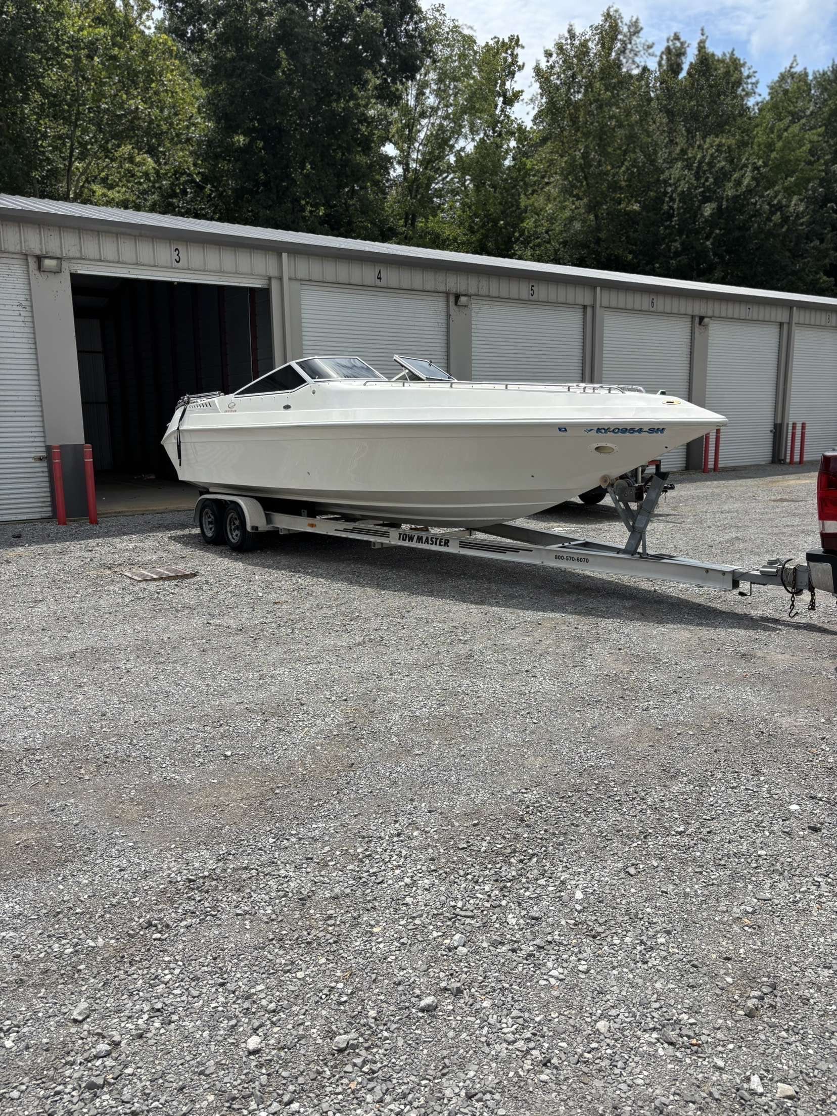 White boat on a trailer parked outside a storage unit.