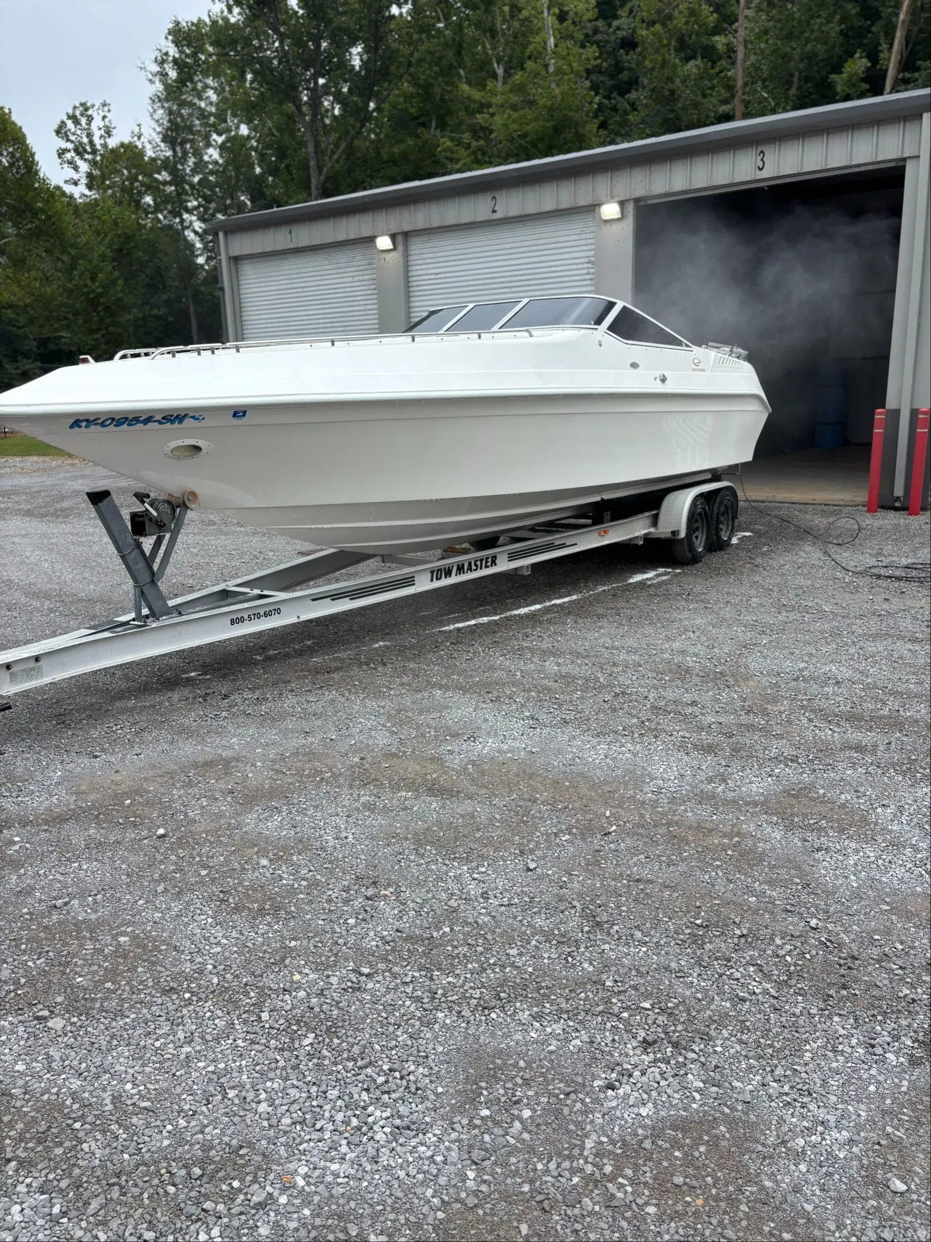 White speedboat on trailer in front of a gray building, visible smoke.