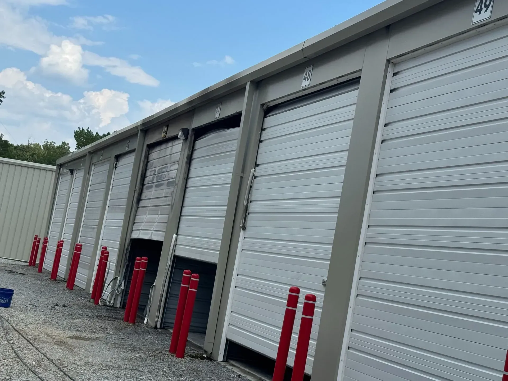 Storage units with gray metal doors, red bollards, and overcast sky.
