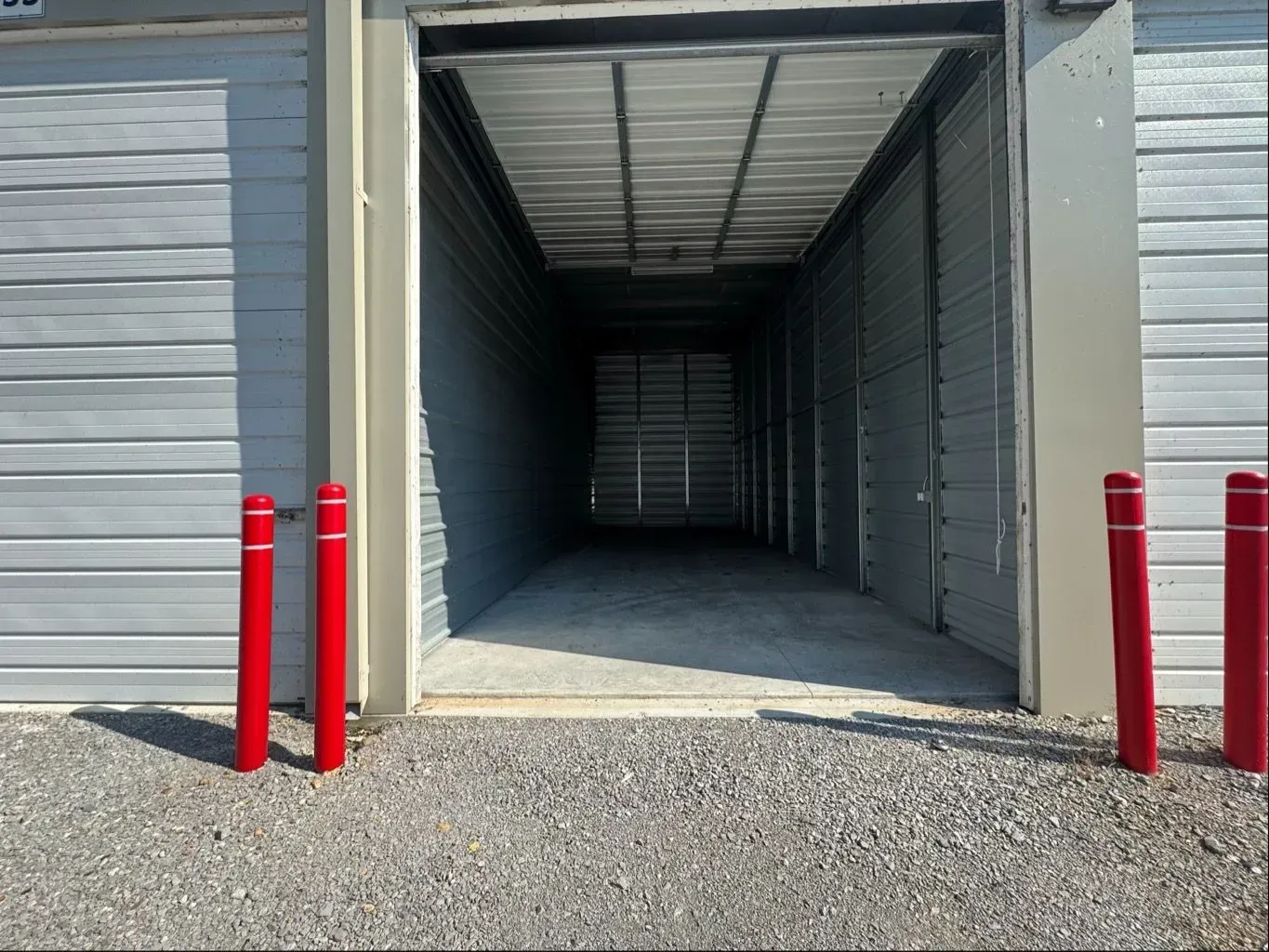 Open storage unit with gravel ground, gray walls, red posts.