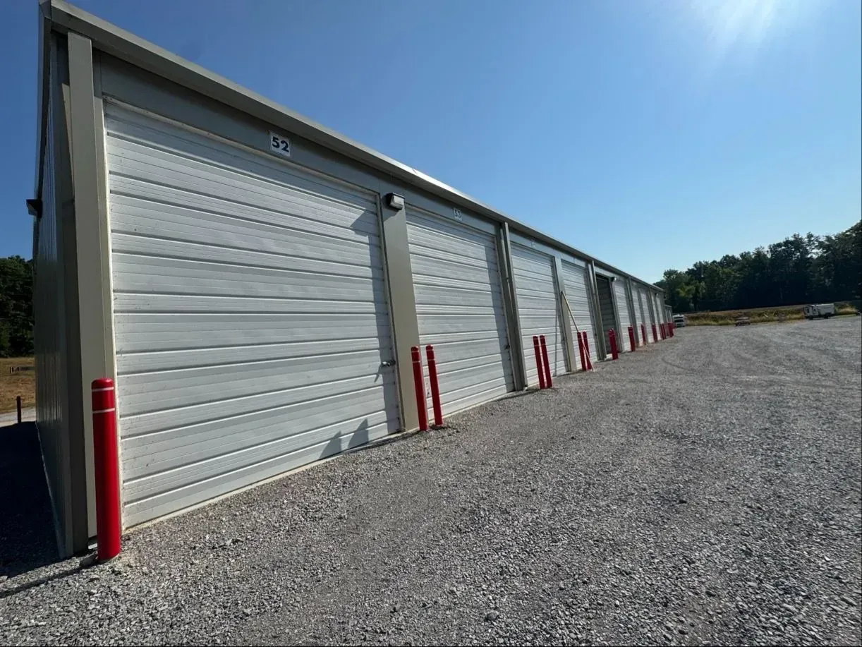 Row of gray storage units under a bright blue sky on a gravel lot.