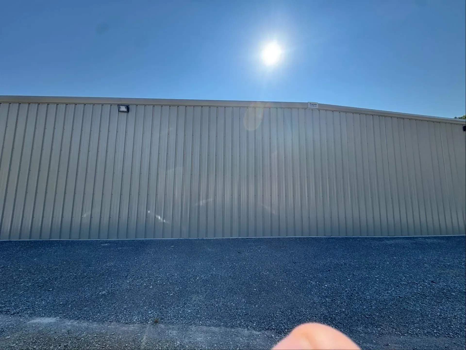 Exterior of a building with vertical siding. Blue gravel in the foreground. Bright sun in a blue sky.
