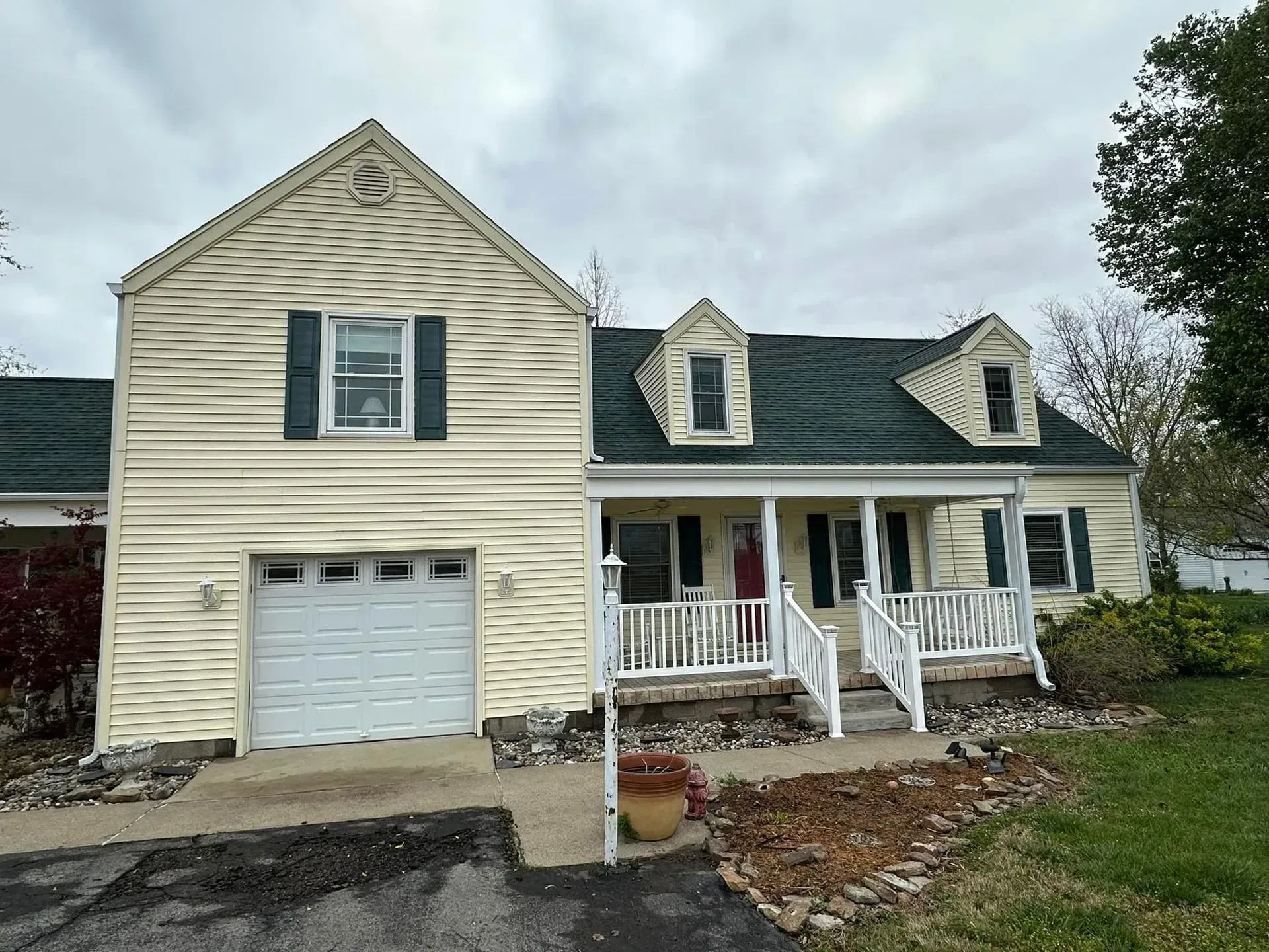 Beige house with a dark green roof, garage, and front porch with white railing.
