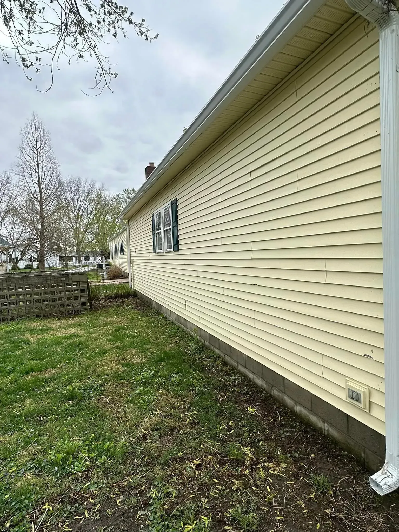Yellow siding on a house with a gutter and downspout. Overcast sky and grassy yard.