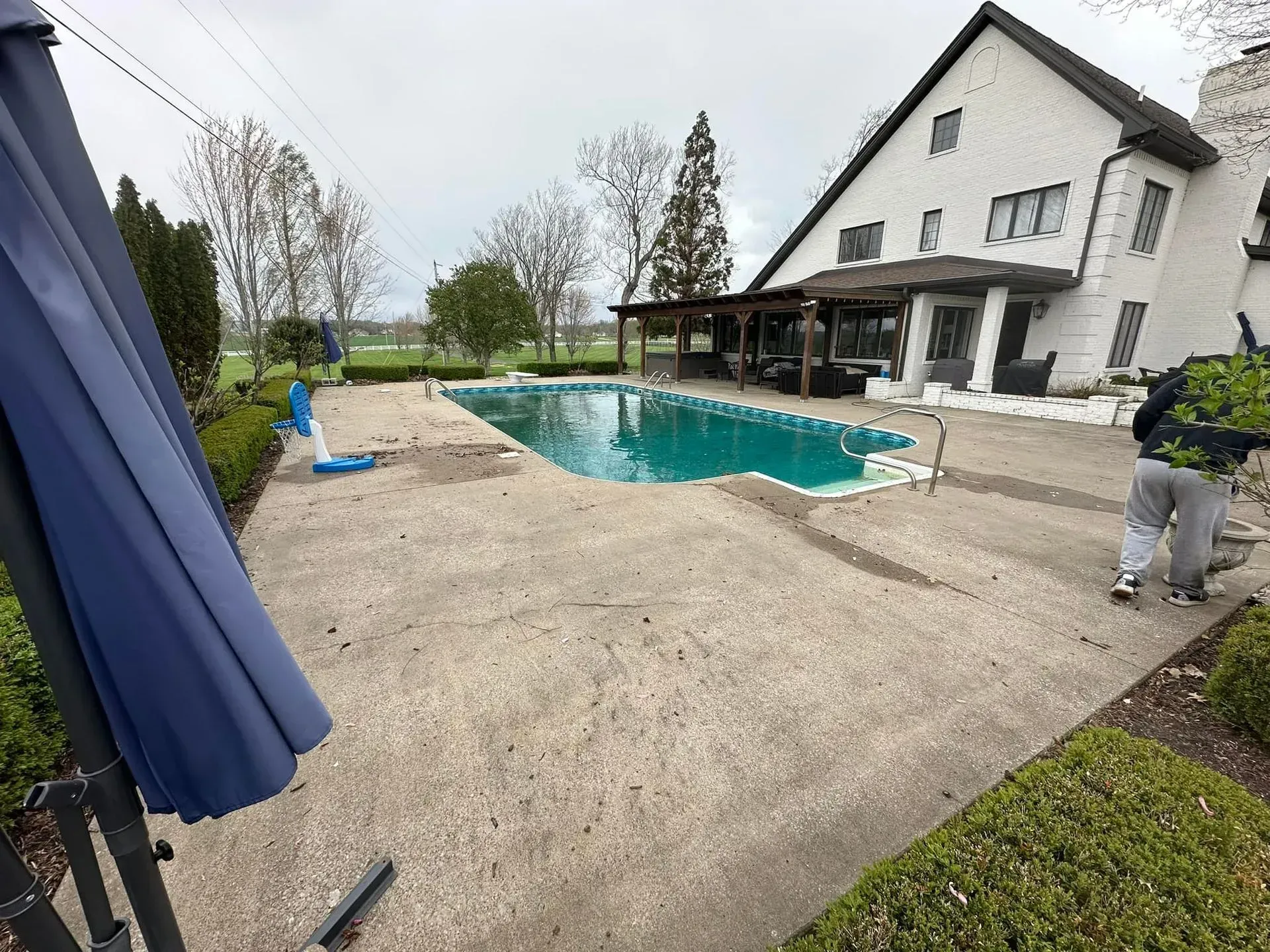 A person by a pool cleaning debris, large house in background, cloudy day.