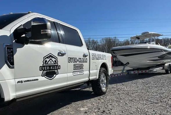 White truck with "Ever-Kleen" logo towing a boat on a trailer in a sunny setting.