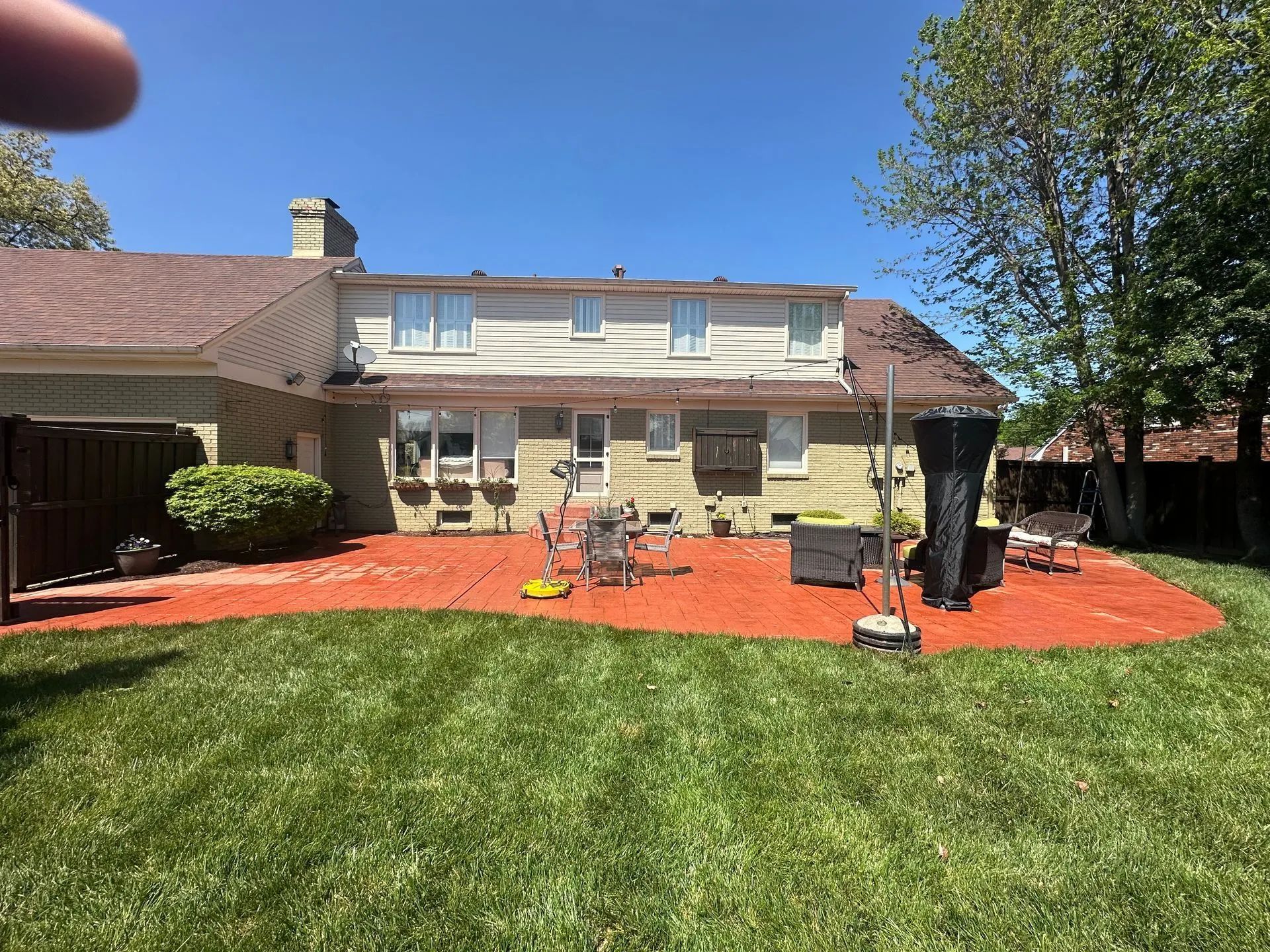 Backyard with red mulch patio, green lawn, beige house, blue sky.