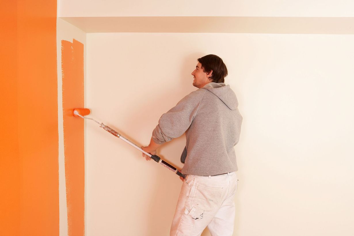 Person painting a white wall with orange paint roller