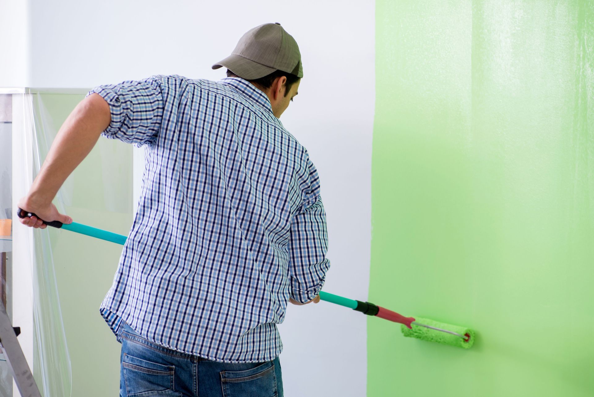 Person painting a wall green with a roller in a bright room