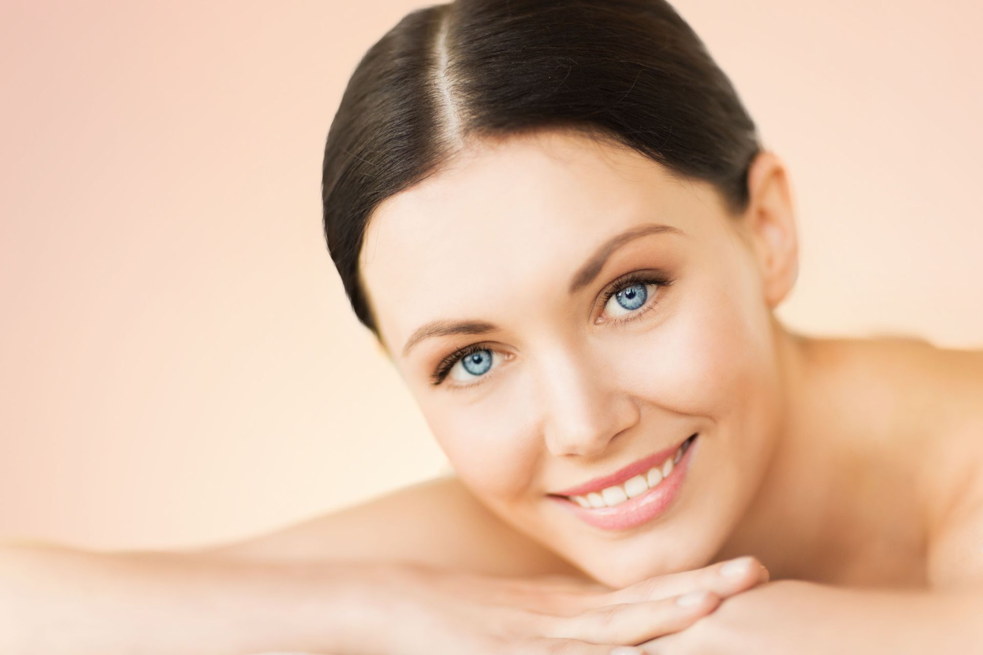 Woman with fair skin and bright blue eyes smiles, resting her head on folded arms.