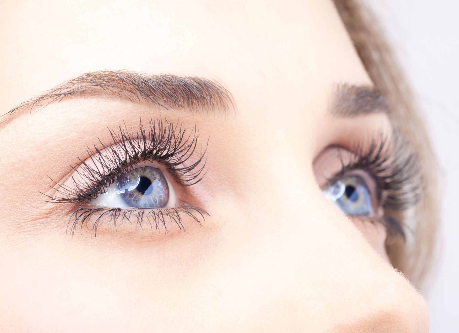 Close-up of a woman's blue eyes looking upwards, with long eyelashes and well-defined eyebrows.