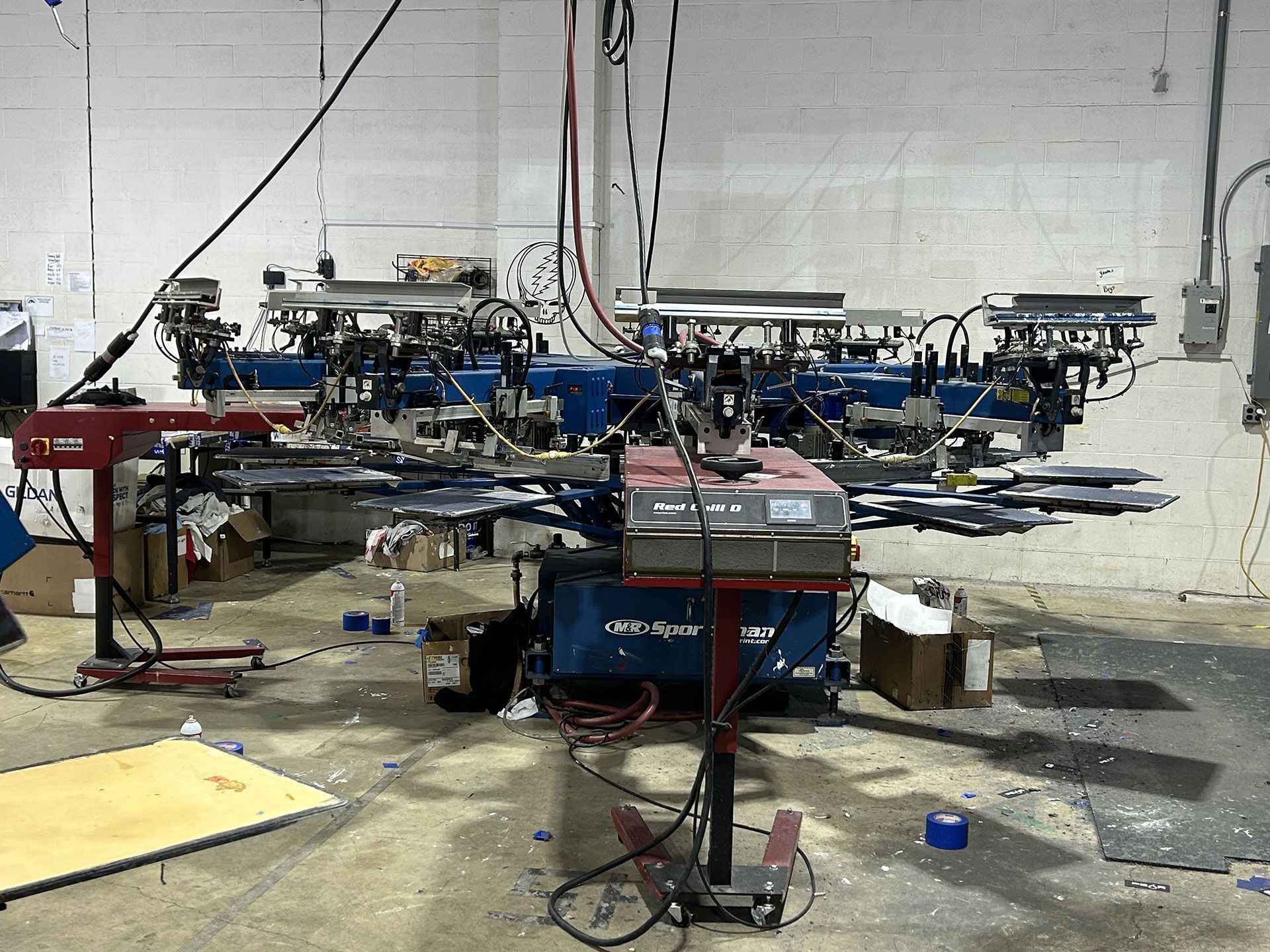 An industrial automatic screen printing press with multiple print stations, set in a warehouse workspace.