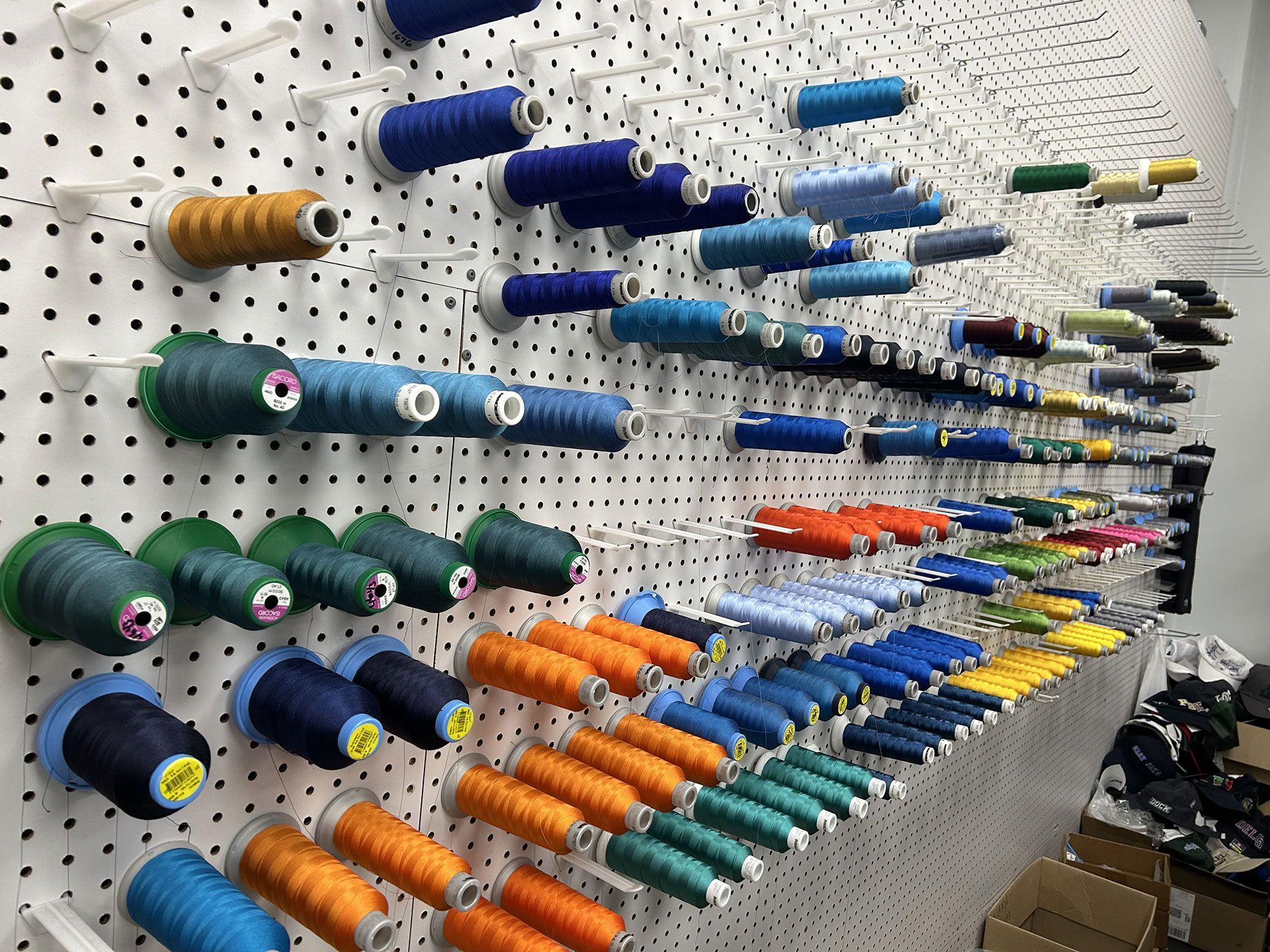 Spools of multicolored sewing thread arranged on a pegboard wall.