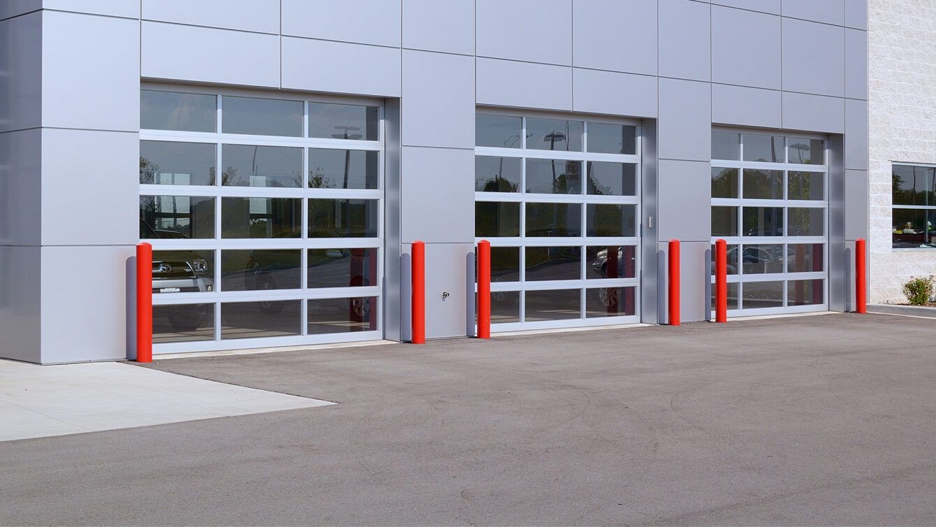 Modern building facade with three garage-style glass doors and red bollards in front