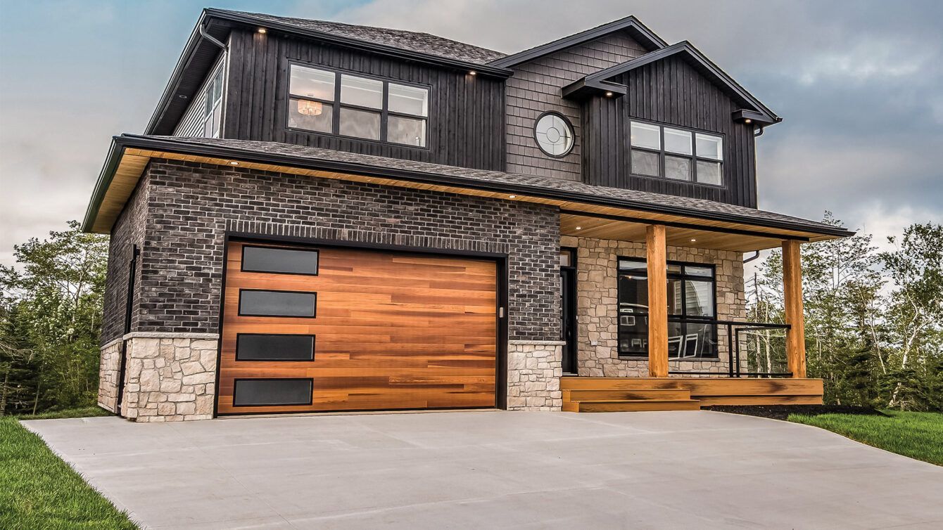Modern two-story house with dark siding, stone accents, and a wood garage door