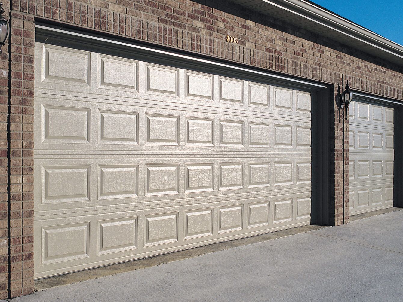 Brick building with two large white garage doors along a paved driveway.