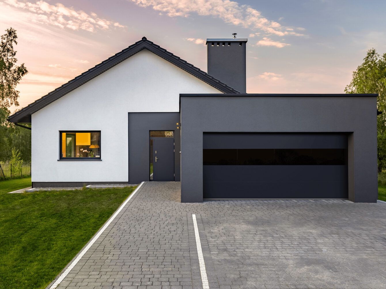 Modern gray-and-white house with a garage and driveway at sunset