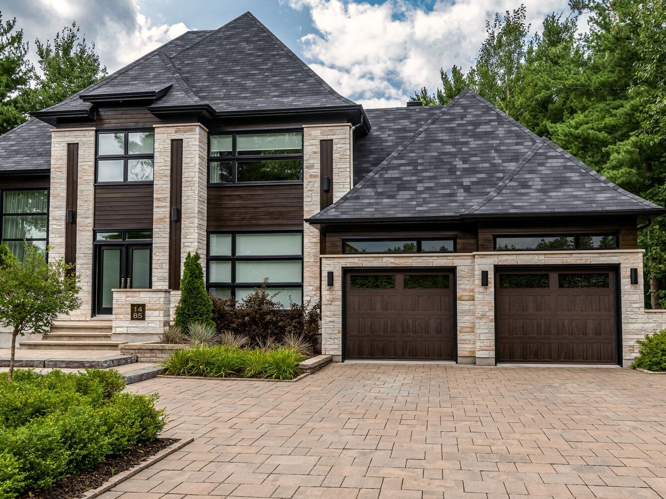 Large modern two-story house with stone facade, dark roof, and a three-car garage under a cloudy sky