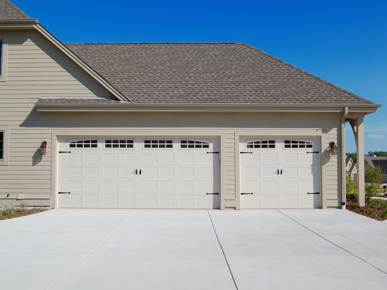 Suburban house exterior with two white garage doors and a wide concrete driveway