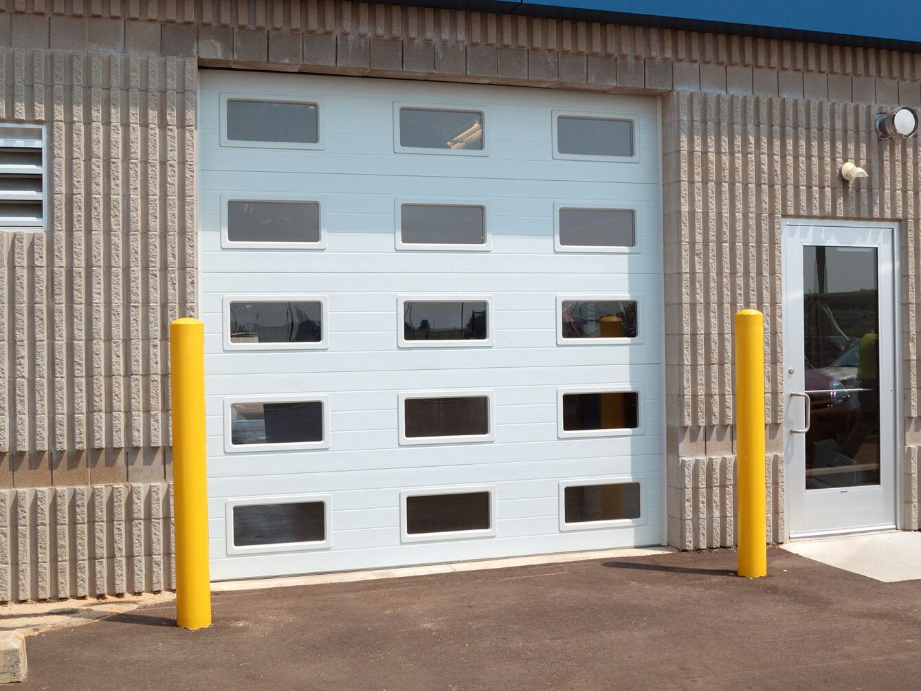 Industrial building exterior with a white garage door, yellow bollards, and a side entrance door
