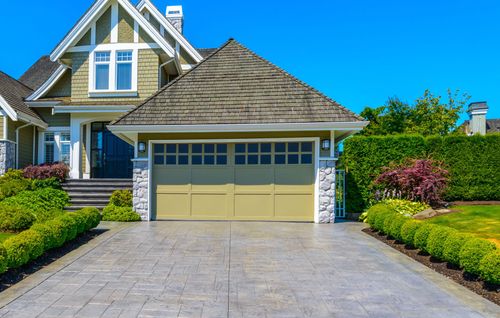 Suburban house with stone garage, landscaped front yard, and wide driveway under a clear blue sky
