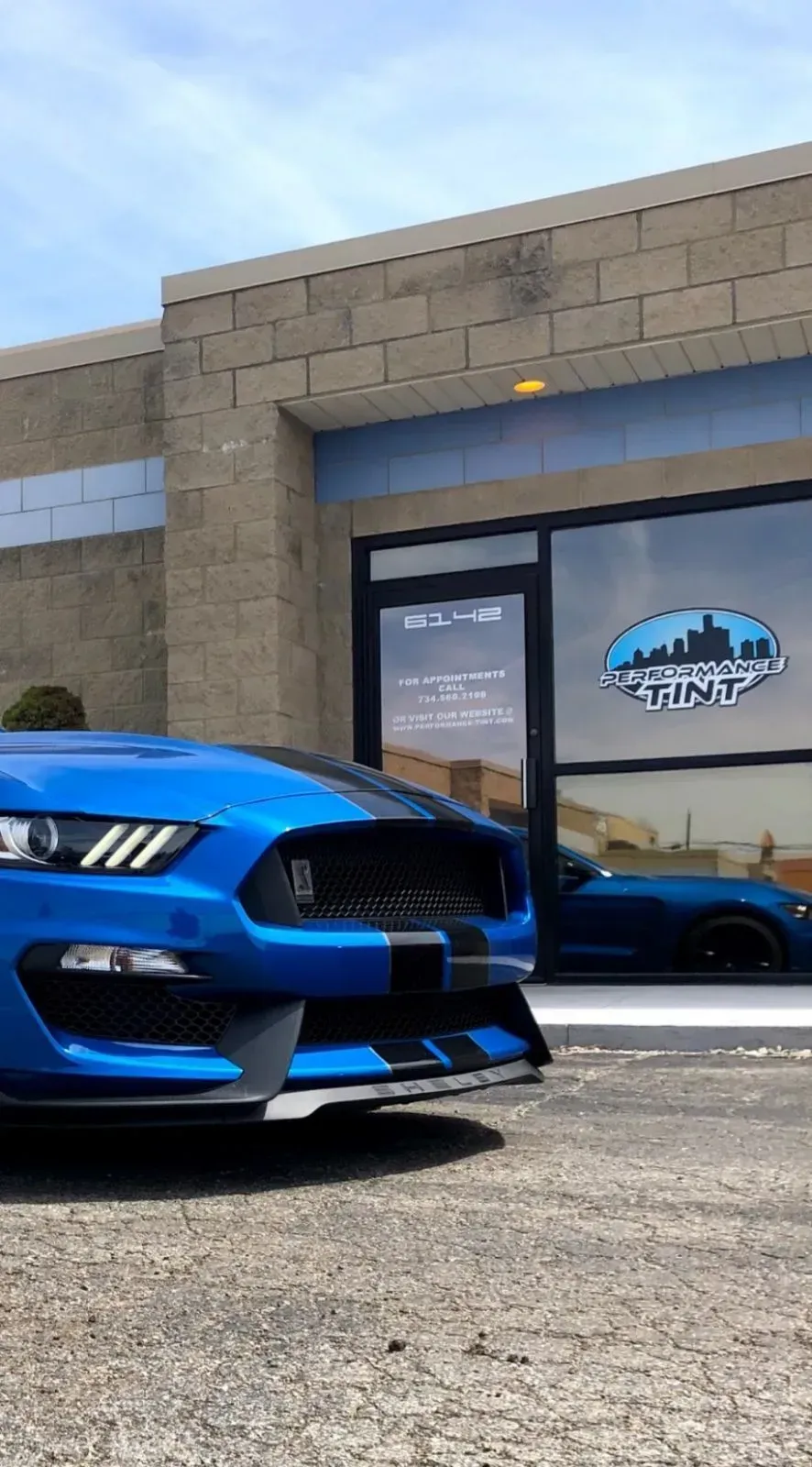 Blue sports car parked outside a building with large glass windows and a logo sign