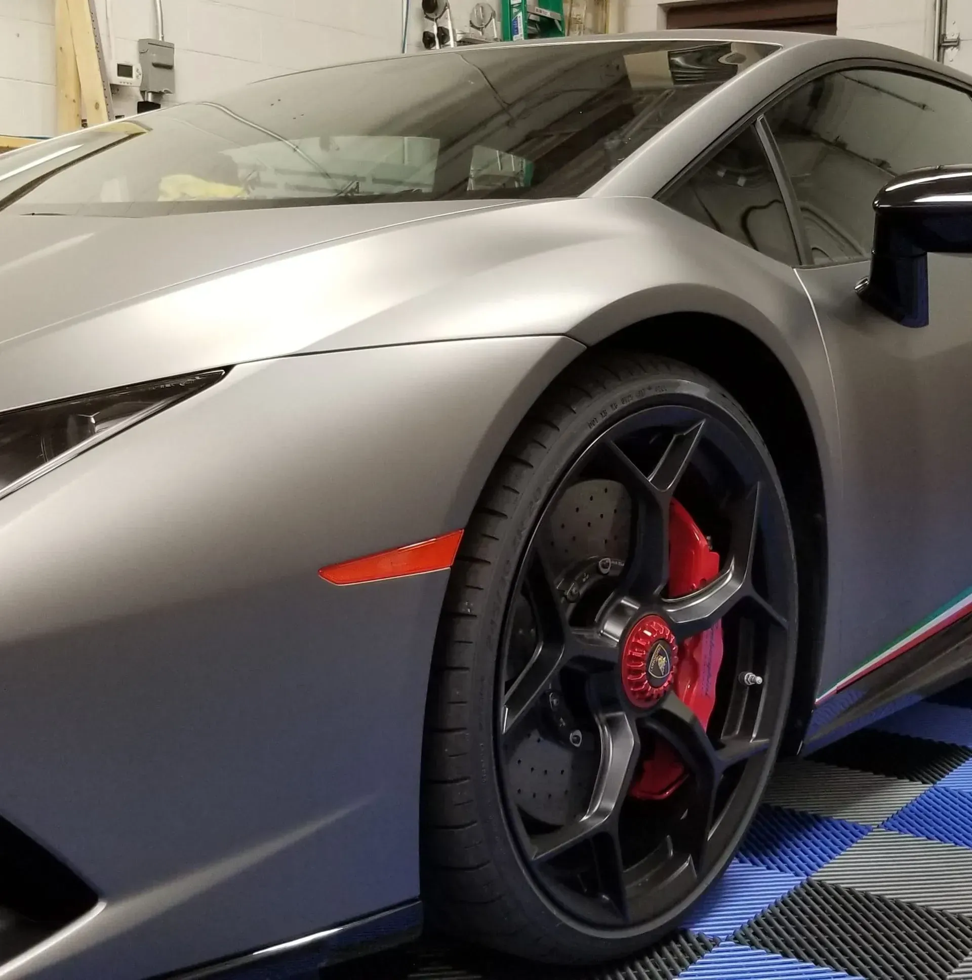 Matte gray sports car parked indoors, showing the front wheel and red brake caliper.