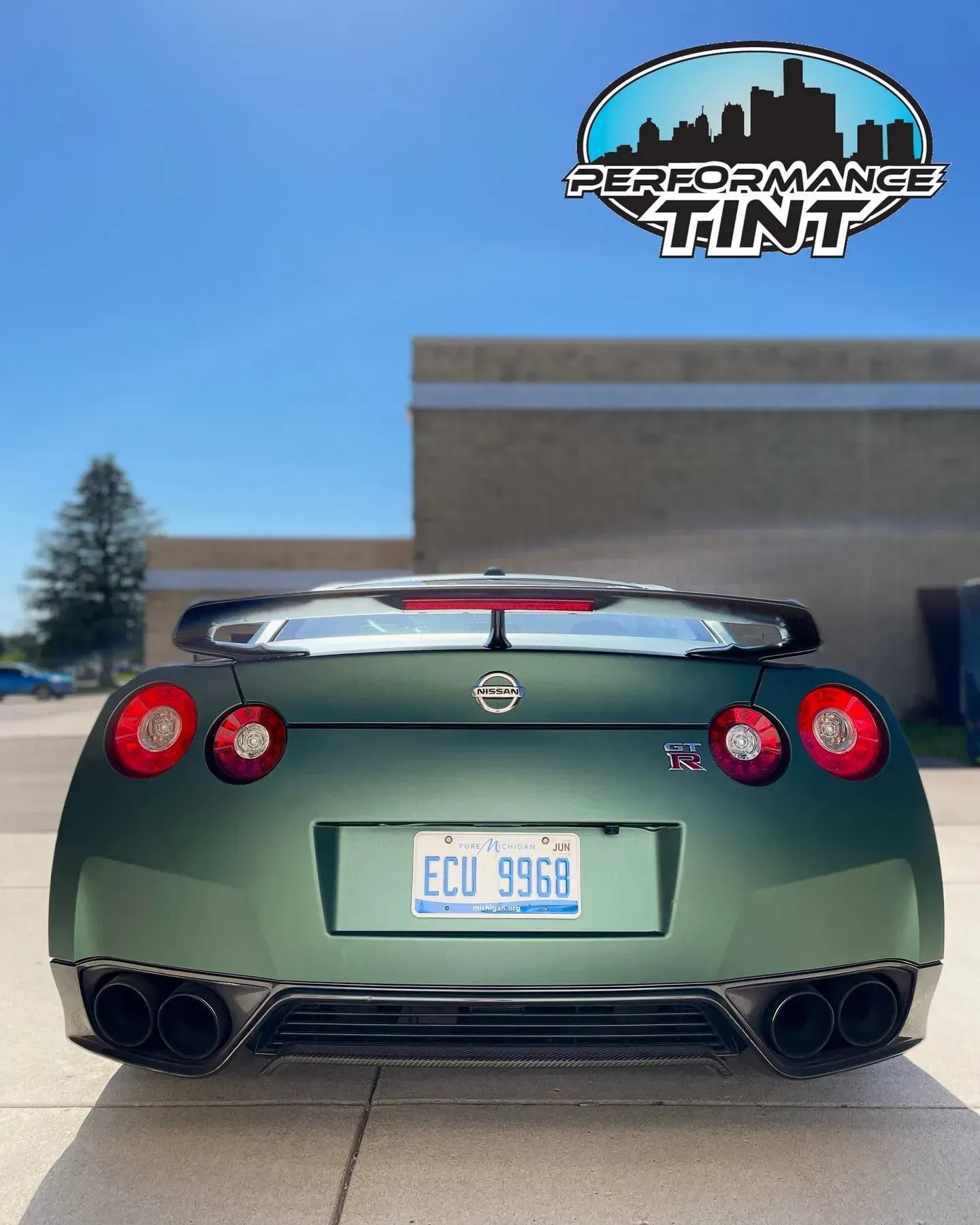 Rear view of a green sports car parked outside a Performance Tint shop under a blue sky