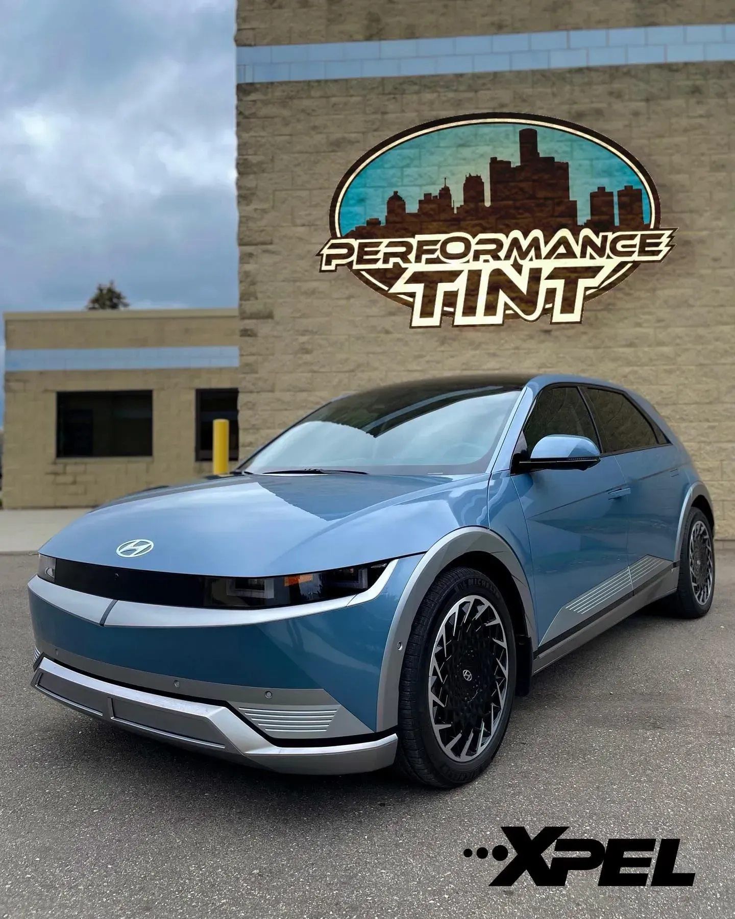 Blue compact SUV parked outside Performance Tint shop with XPEL logo on the wall
