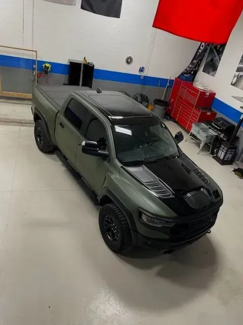 Matte green pickup truck with black hood in an indoor garage, viewed from above.