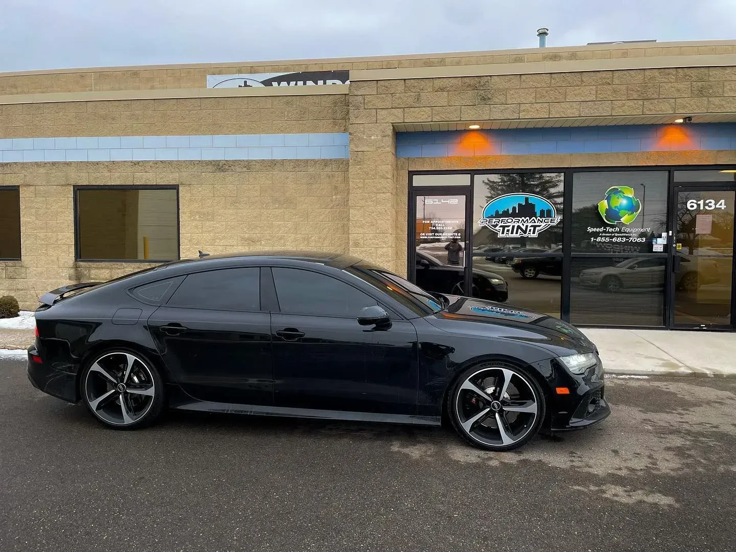 Black sports sedan parked outside a brick storefront with lit windows on a rainy day