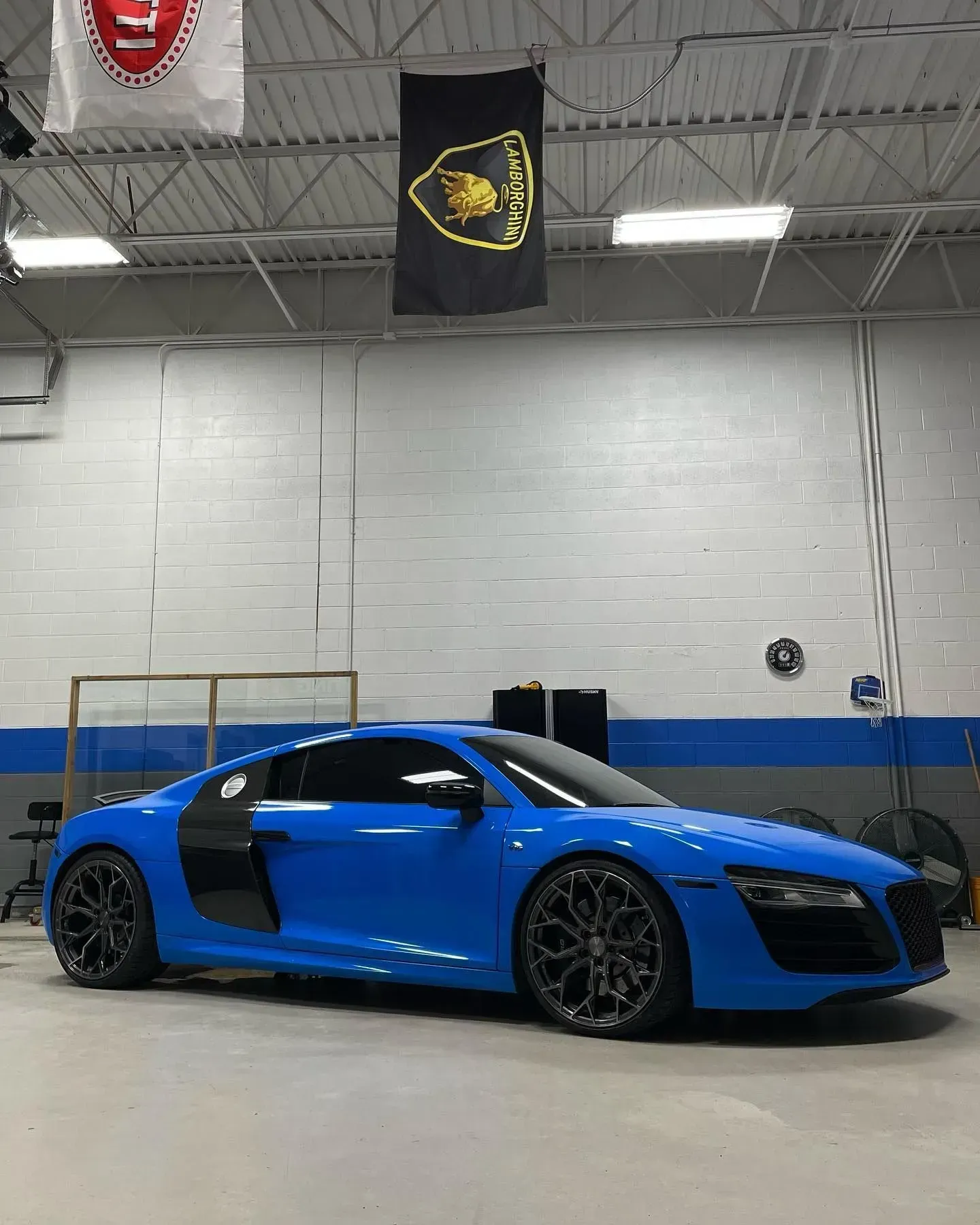 Blue sports car parked in an indoor garage, shown in side view with black rims.