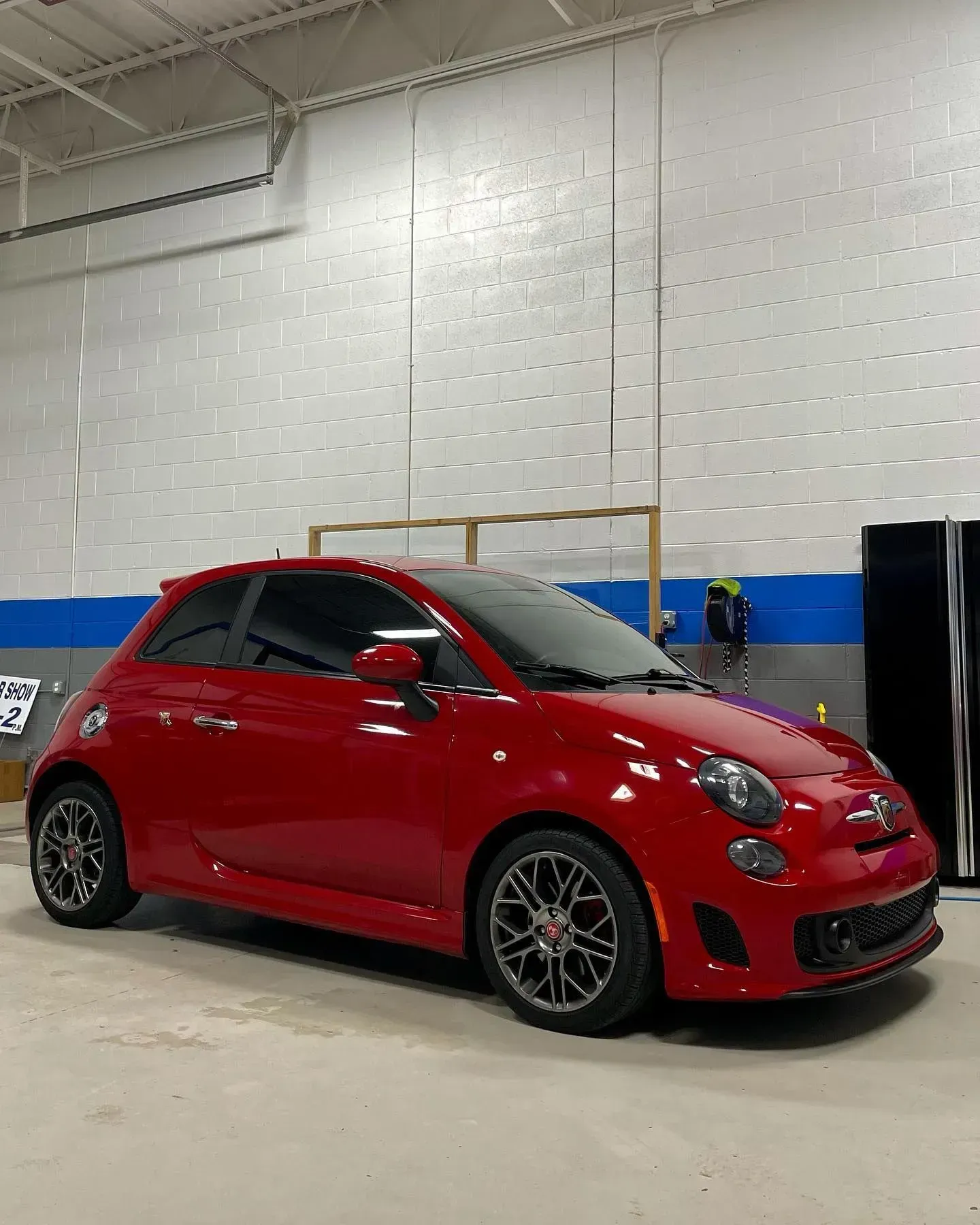 Red compact car indoors on a showroom floor, shown in three-quarter front view.