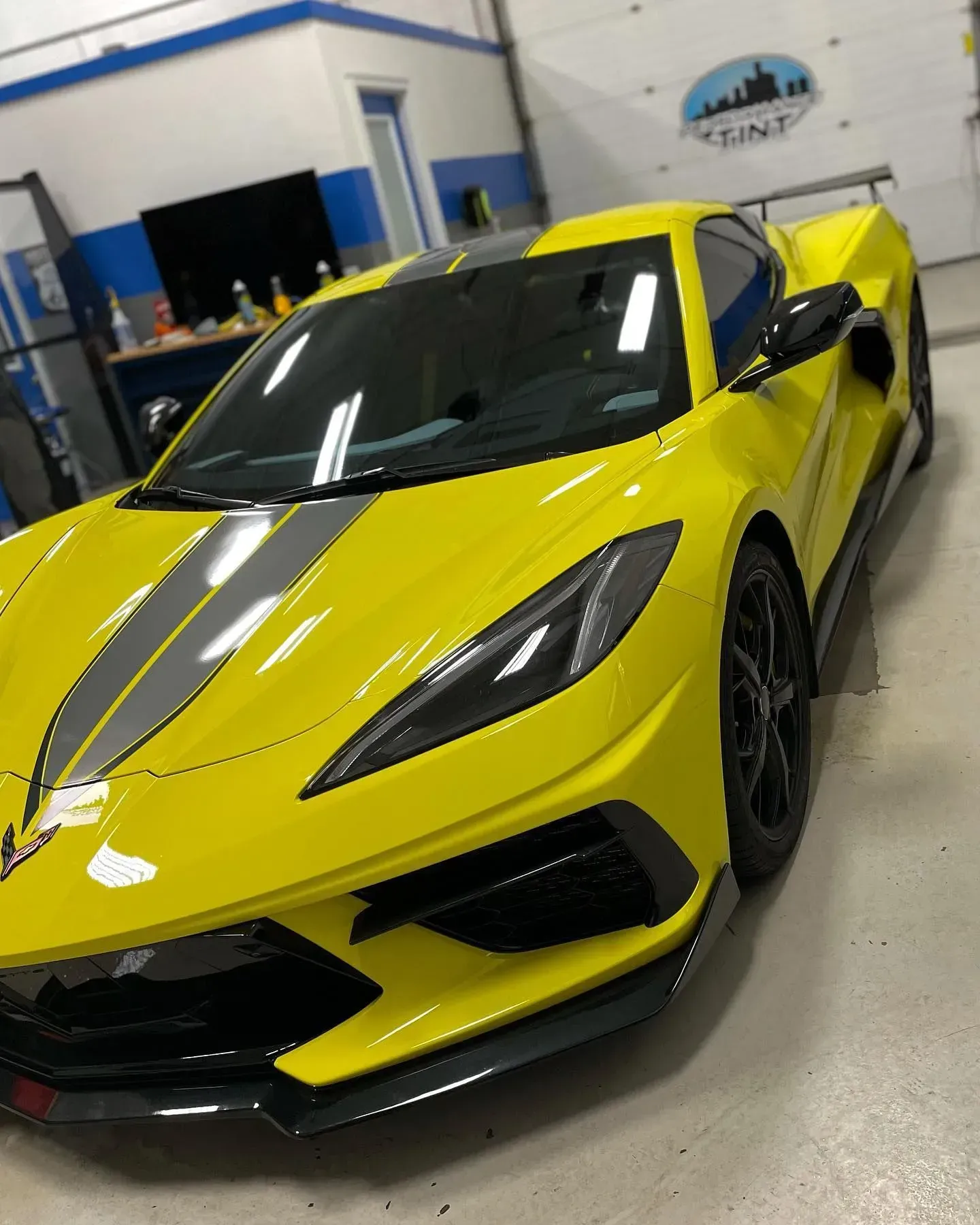 Bright yellow sports car with black racing stripes parked indoors in a garage