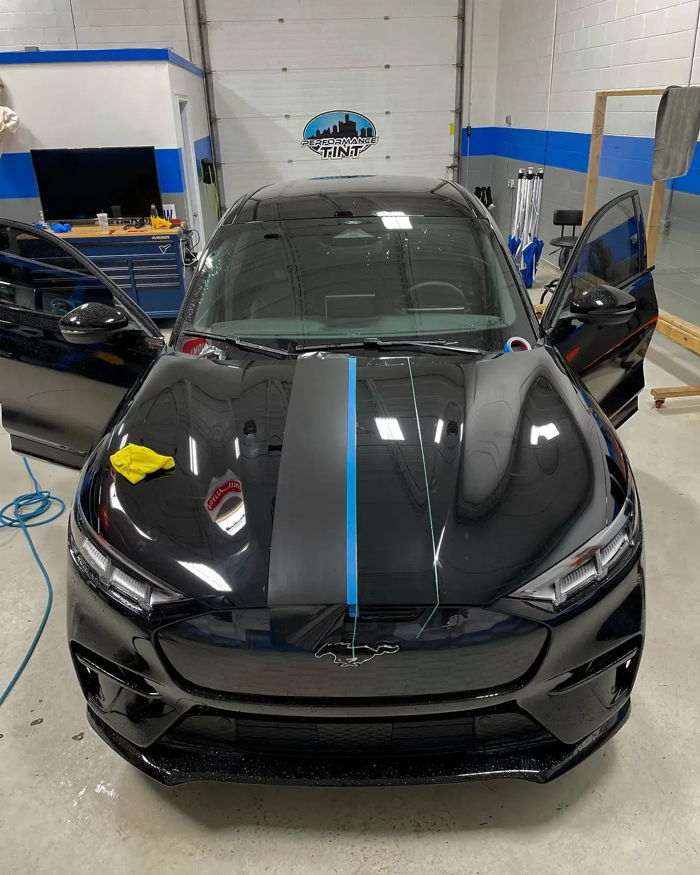 Black sports car in an auto shop, front view with doors open and a blue stripe on the hood.