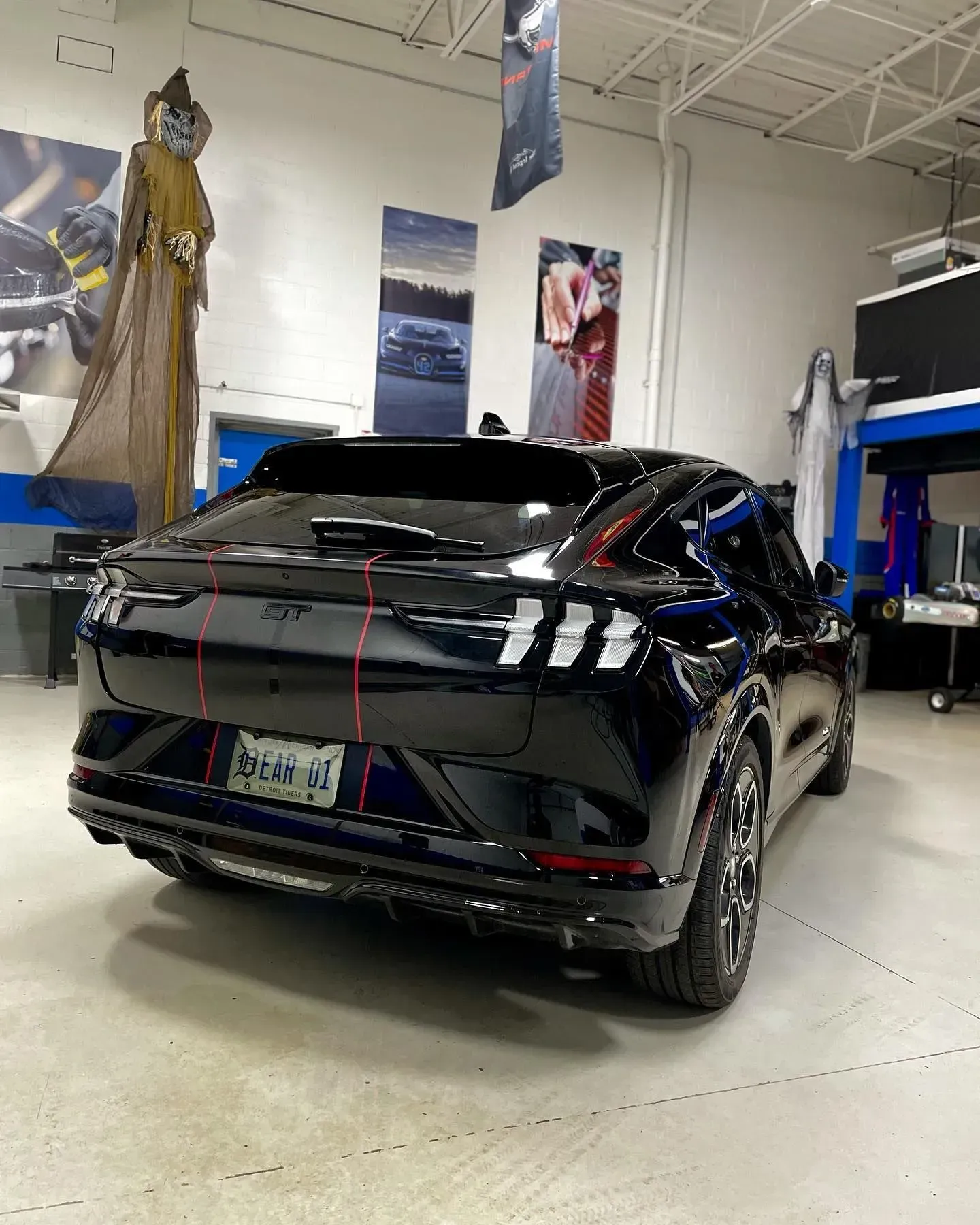 Black SUV in an auto shop, viewed from the rear with red tape on the body.