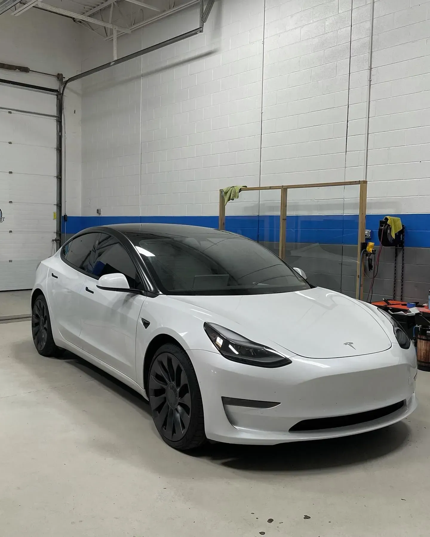 White Tesla sedan parked inside a garage with white walls and blue stripe