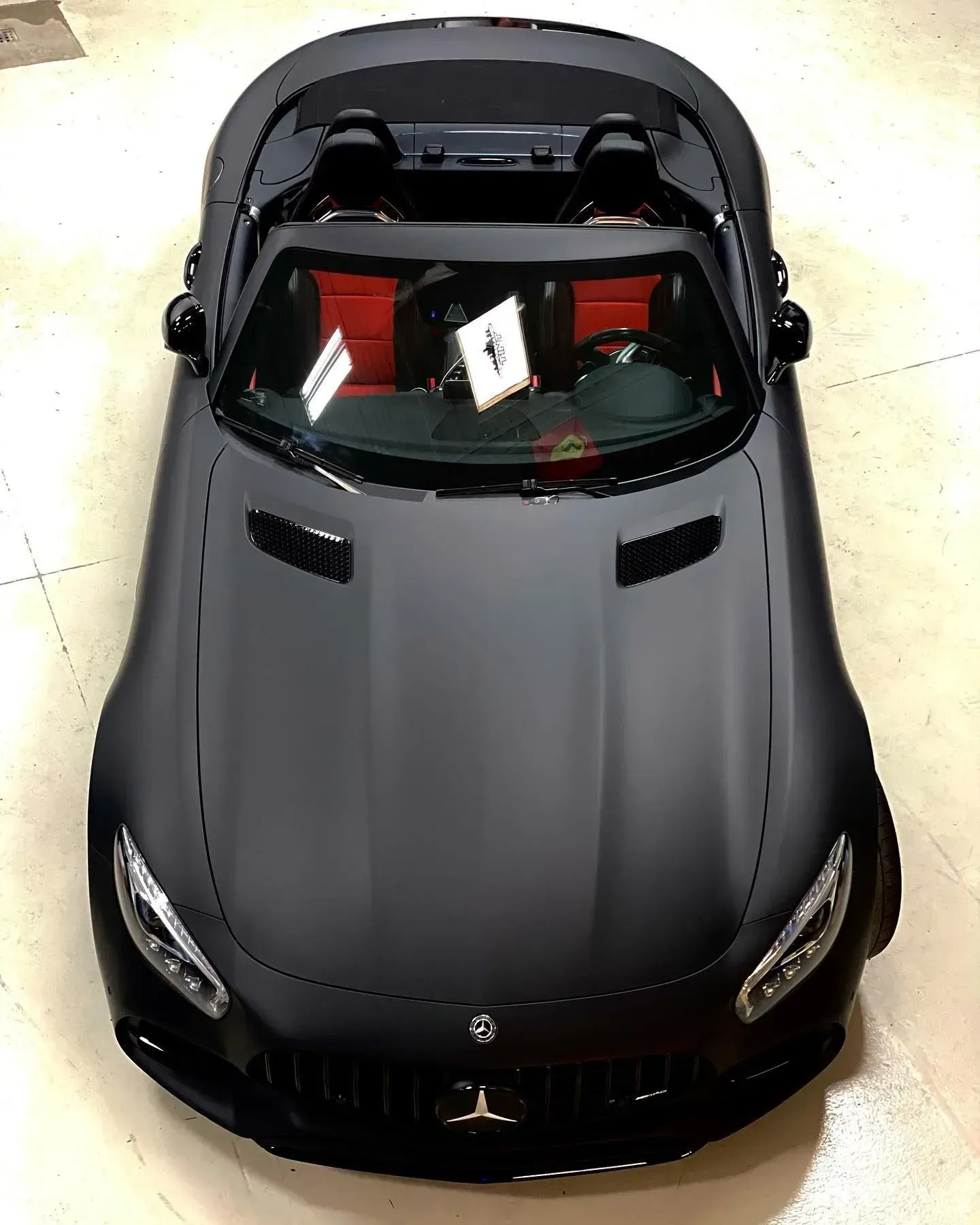 Black convertible sports car viewed from above, parked indoors with the roof down.