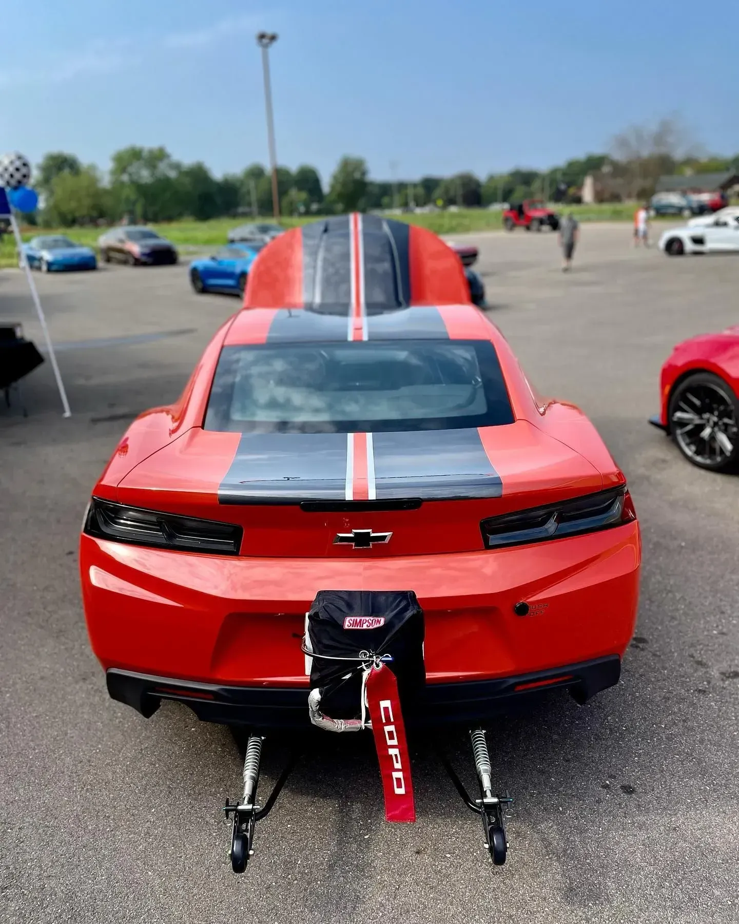 Red Chevrolet Camaro with racing stripes and front splitter at an outdoor car show