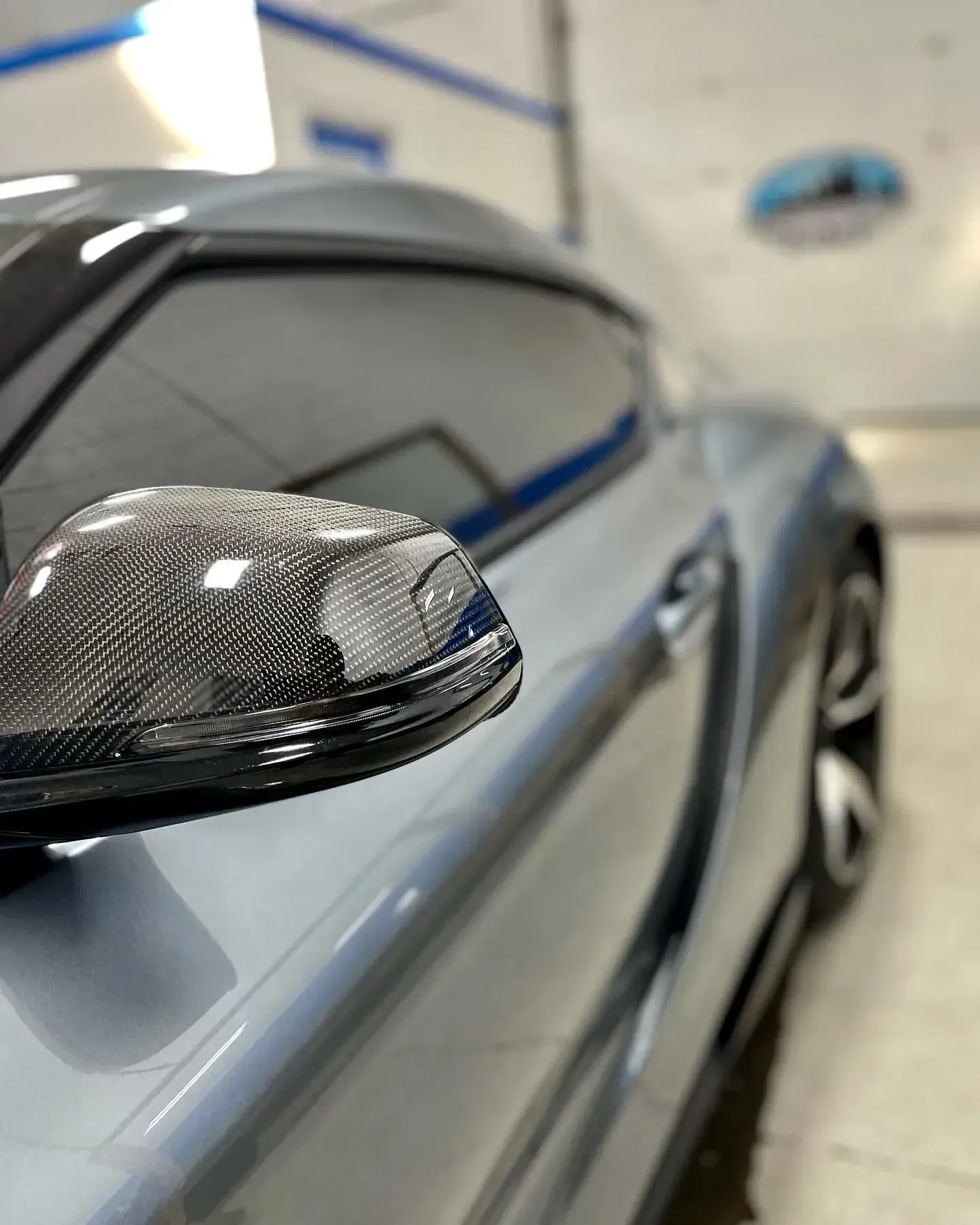 Close-up of a blue sports car with a carbon-fiber side mirror in a garage