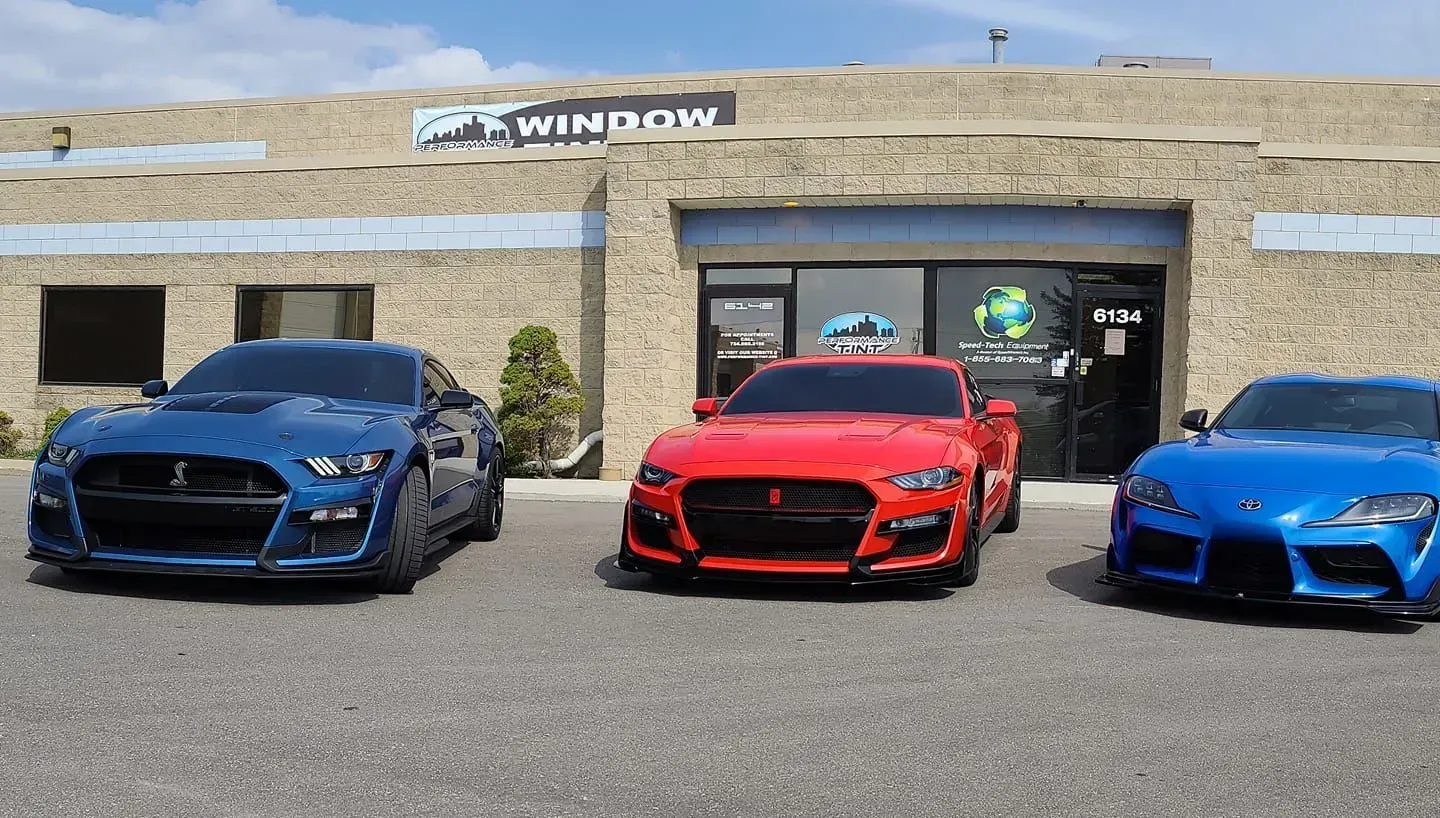 Three sports cars—blue, red, and blue—parked outside a Windy City dealership.