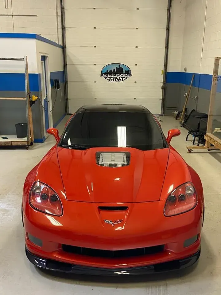 Red sports car in a garage, front view, with black hood and bright orange body.