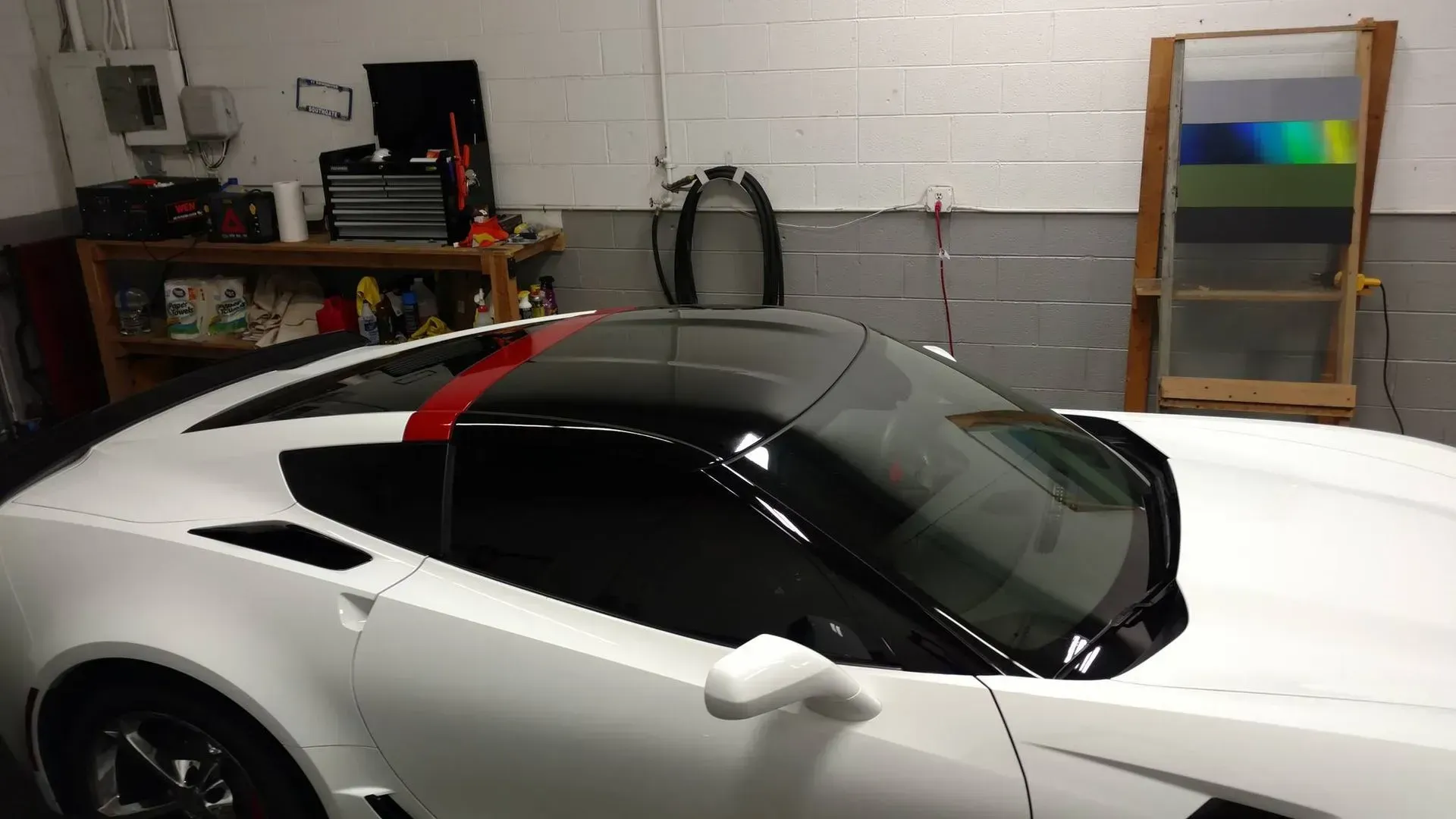 White sports car with tinted windows in a garage, with a workbench and shelving in the background