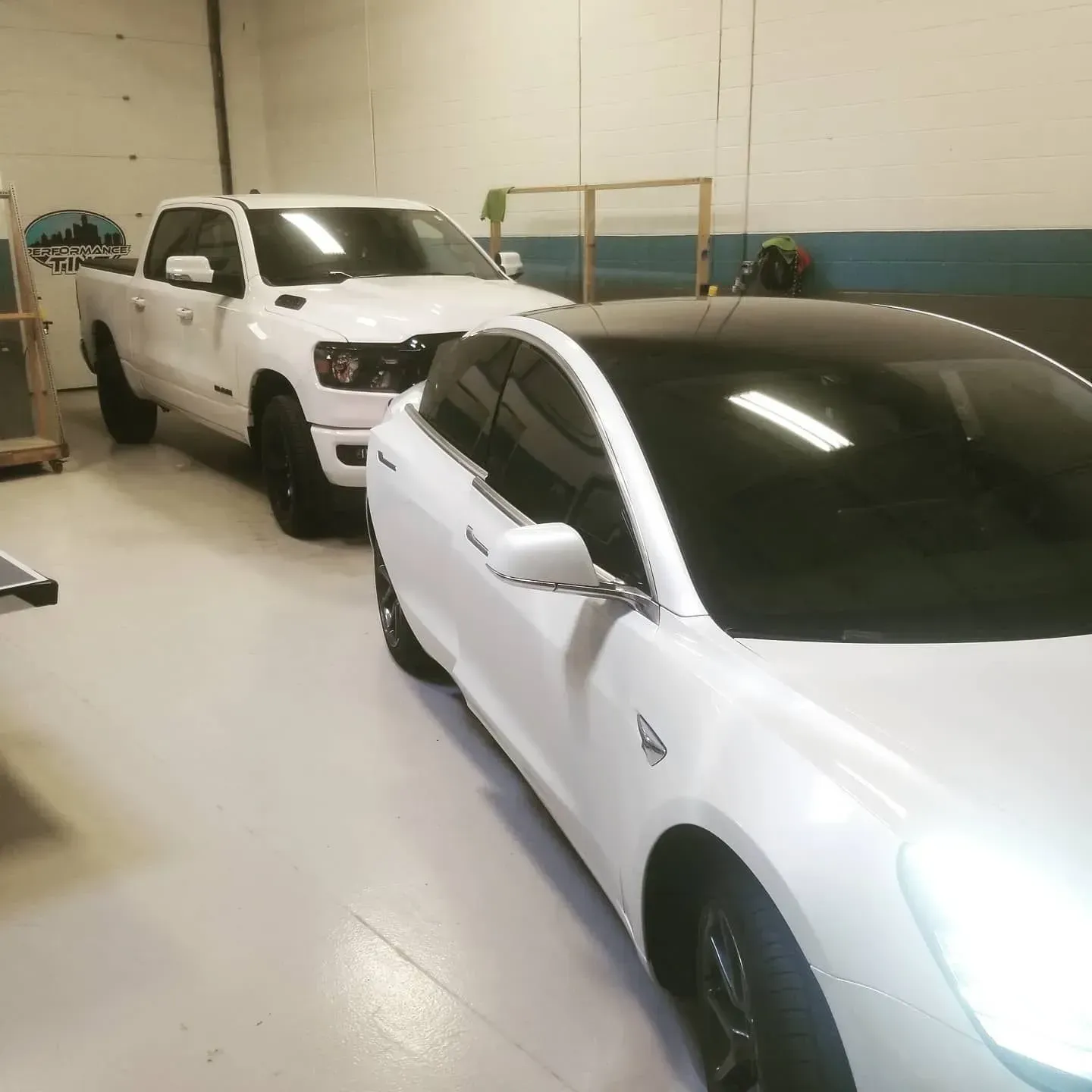White sedan parked in a garage, with a white pickup truck behind it.
